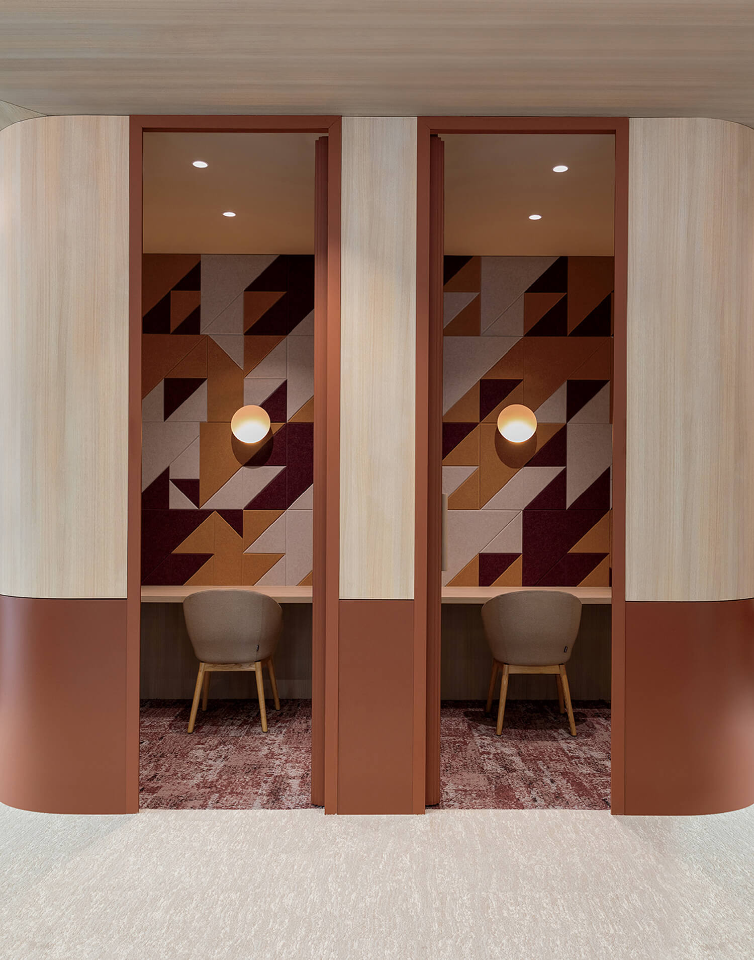 Two small work booths with geometric patterned walls, round wall lights, and beige chairs separated by a partition in a modern office setting.