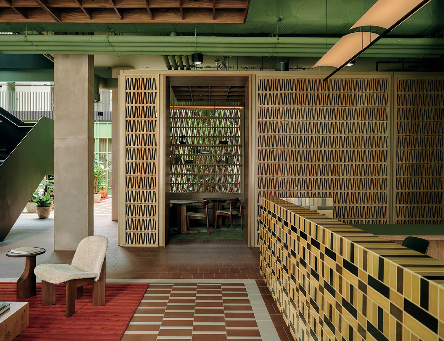 Modern interior with geometric tile patterns, a green ceiling, wooden furniture, a checkered reception desk, and a partition with a diamond cutout design.