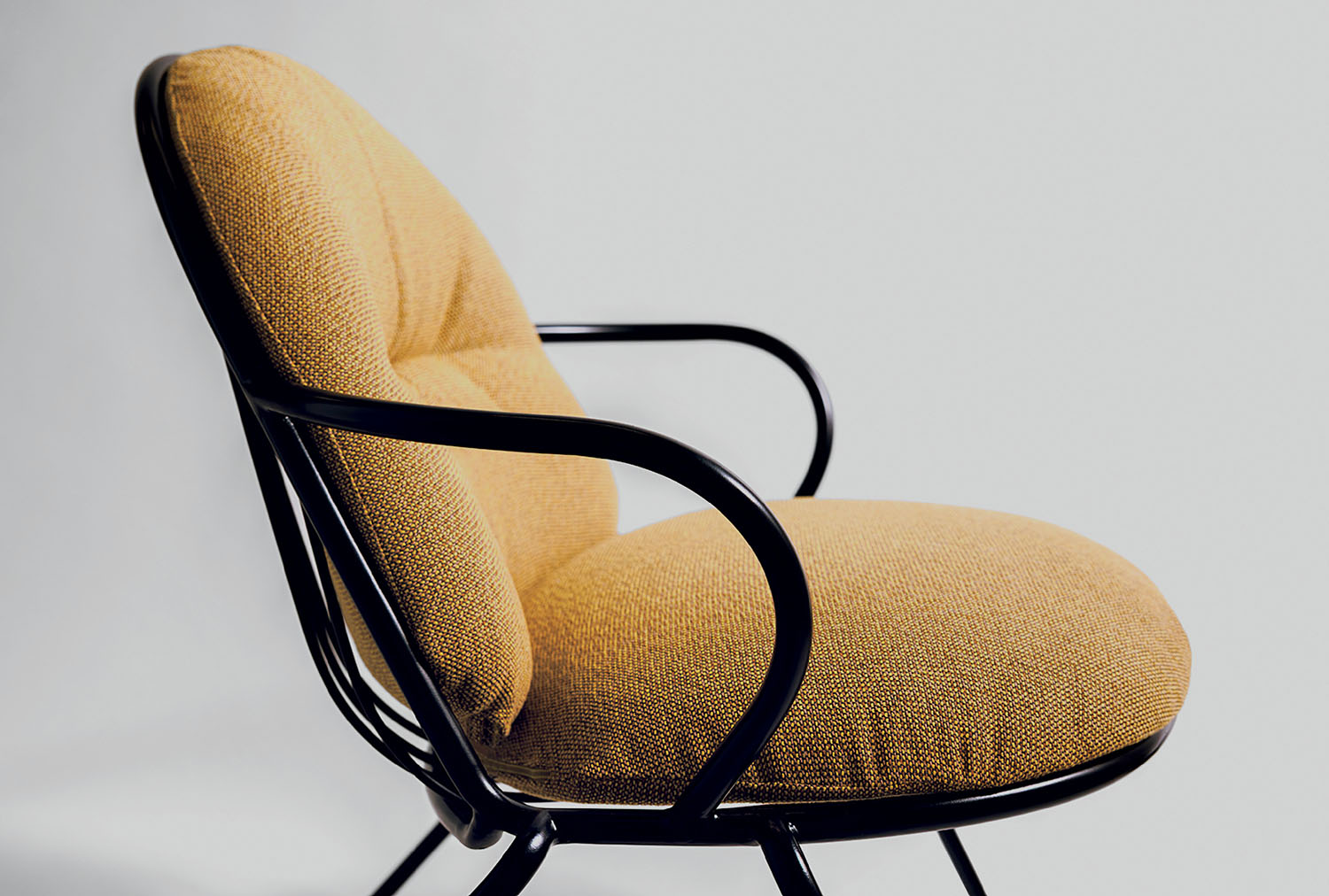 A mustard-colored cushioned chair with black metal armrests and frame, photographed against a plain light background.