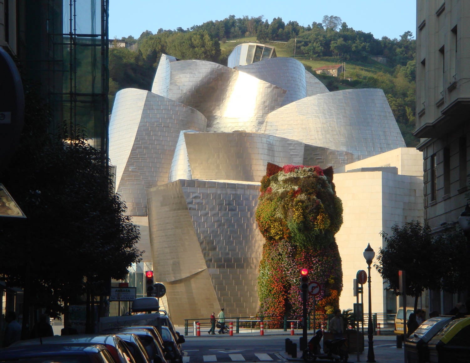 The Guggenheim Museum Bilbao’s metallic, curving exterior with a large floral sculpture shaped like a dog in front, seen from a city street.