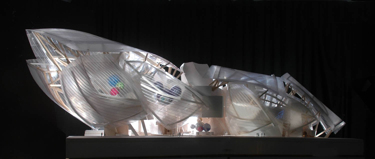 Architectural model of a futuristic building with translucent, curved surfaces and exposed structural elements, displayed against a dark background.
