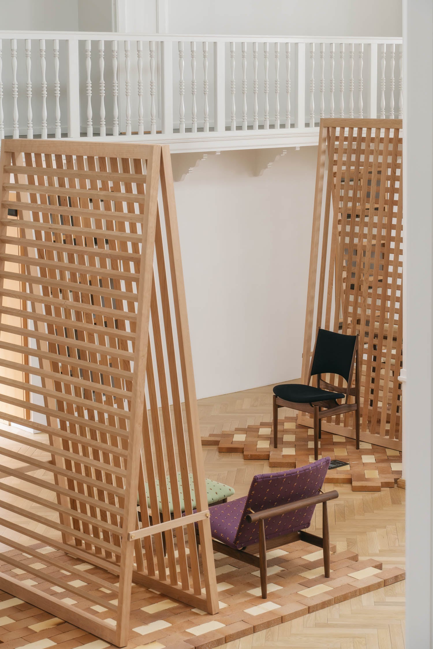 Two wooden lattice room dividers stand in a bright space with parquet flooring, accompanied by a black chair and a purple-patterned armchair.