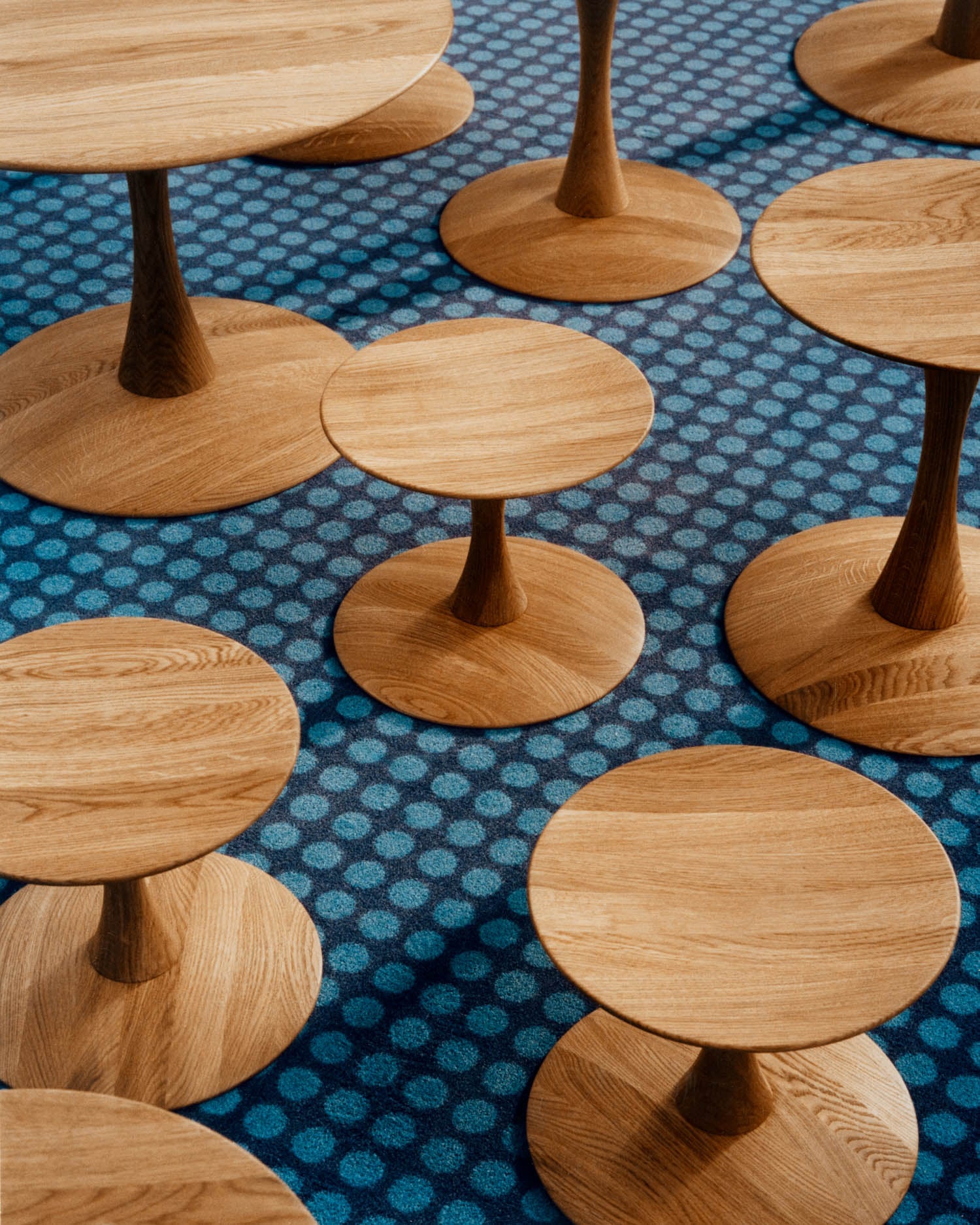 Several round wooden tables with pedestal bases are arranged on a blue, polka-dotted carpet.