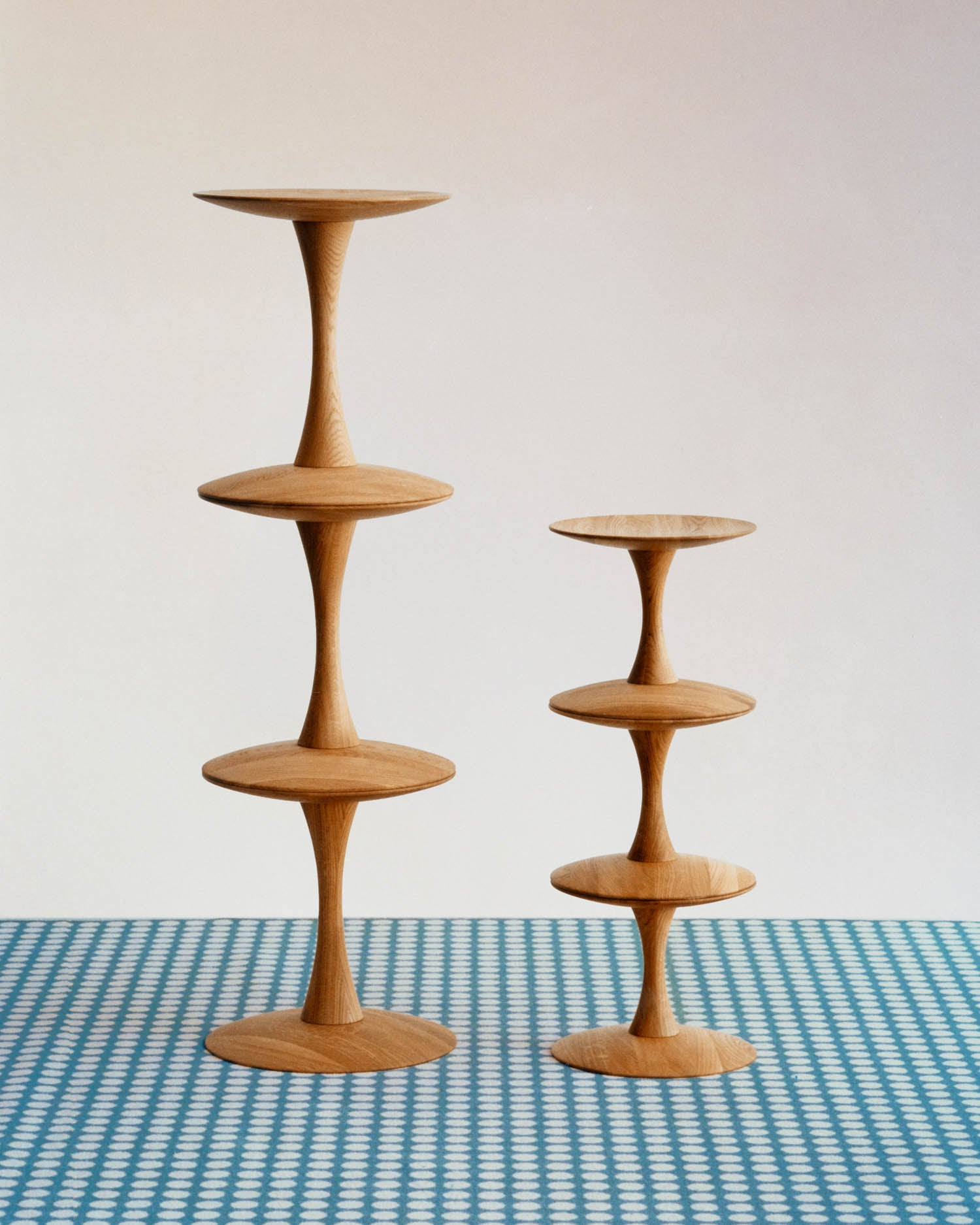 Two wooden tiered stands of different heights are displayed on a blue and white patterned surface against a plain background.