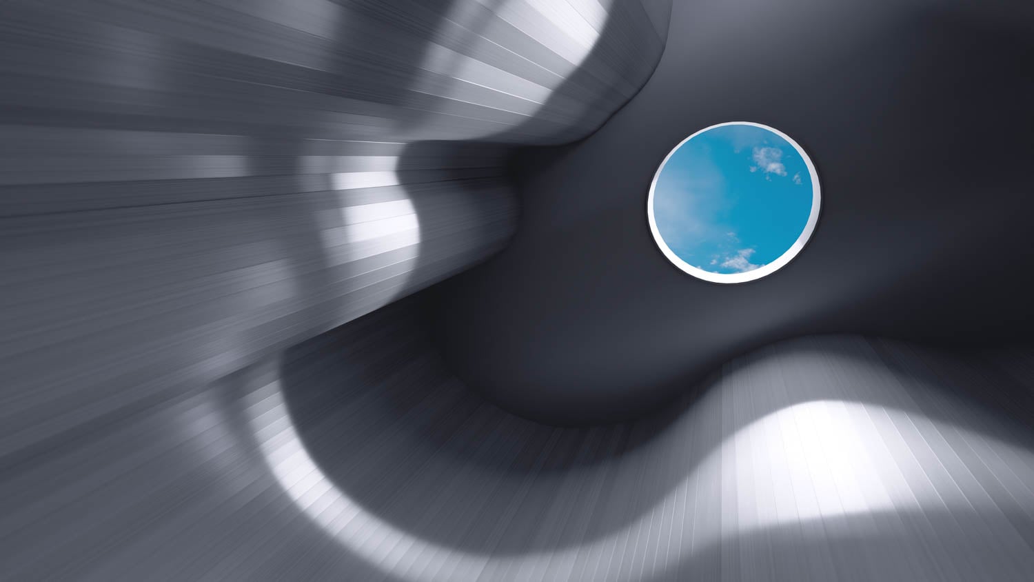 A round skylight in a smooth, curved metallic ceiling reveals a view of blue sky and clouds. Light and shadows create abstract patterns on the surface.