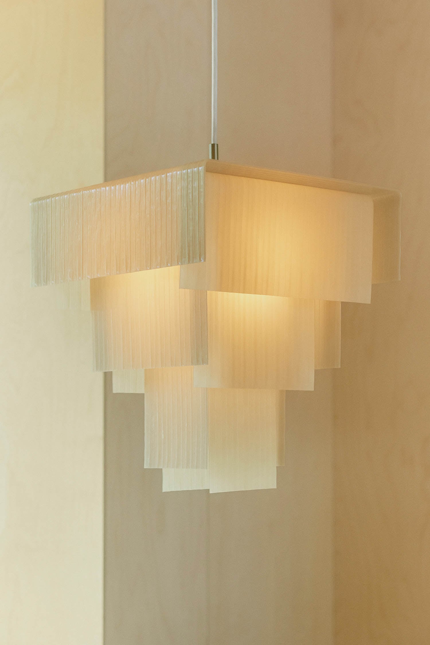 A pendant light fixture with layered, translucent rectangular panels emits a warm glow against a light wood background.