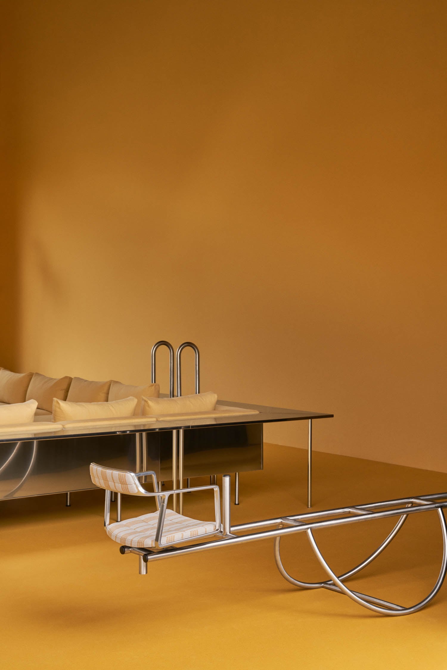 Minimalist room with mustard yellow walls and floor, featuring a metal-framed bench, a matching chair, and a sofa with cream cushions.