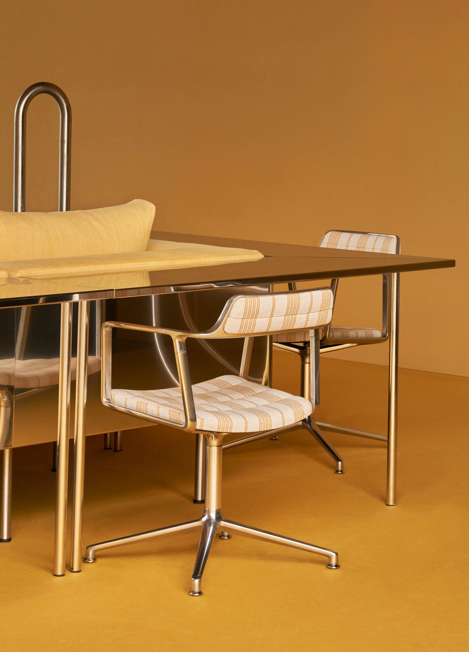 A modern dining table with a reflective surface, metal legs, and two striped cushioned chairs on wheels, set against a yellow background.