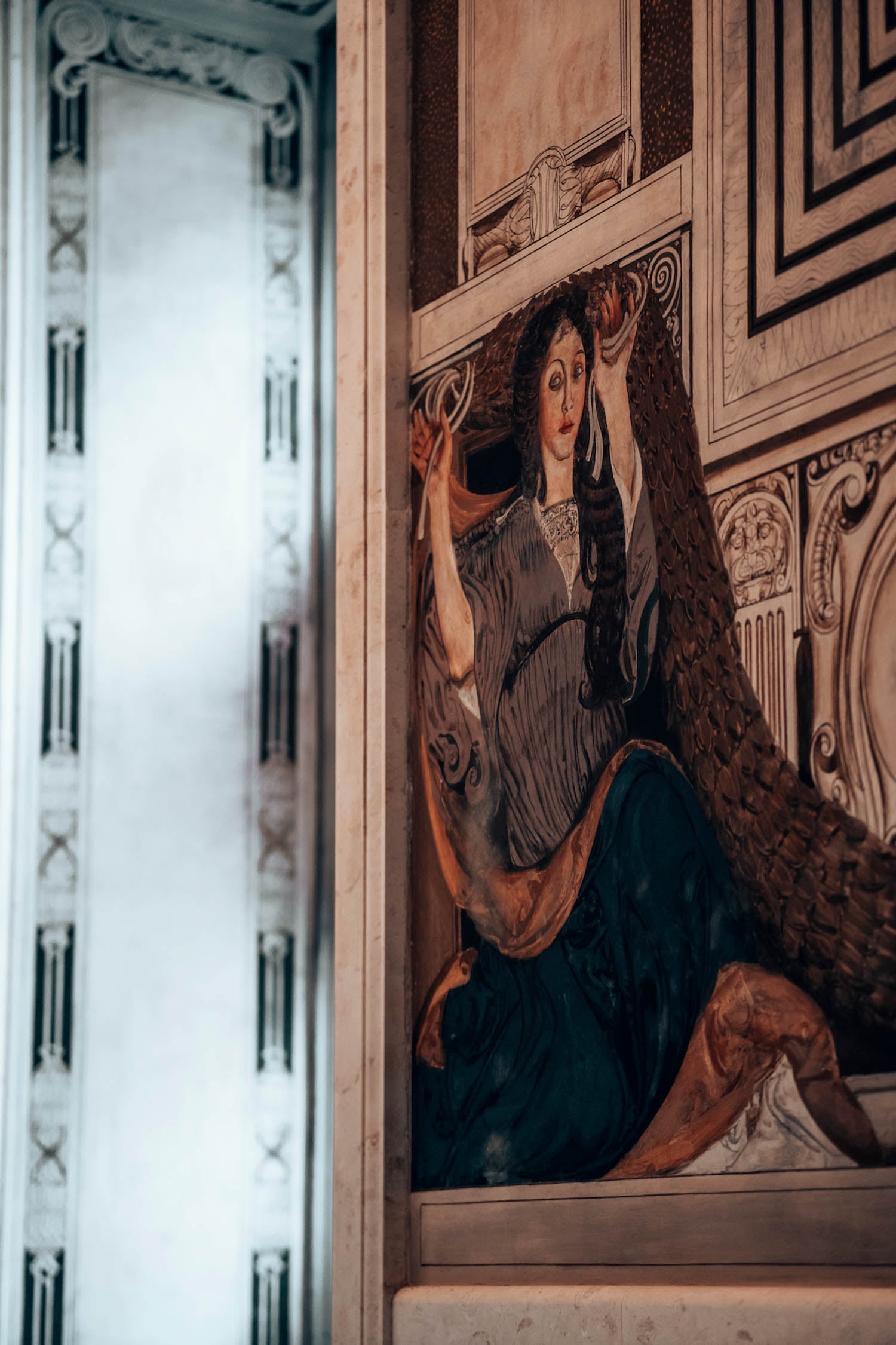 A mural depicts a seated woman in medieval-style clothing holding an object above her head, set against an ornate architectural background.