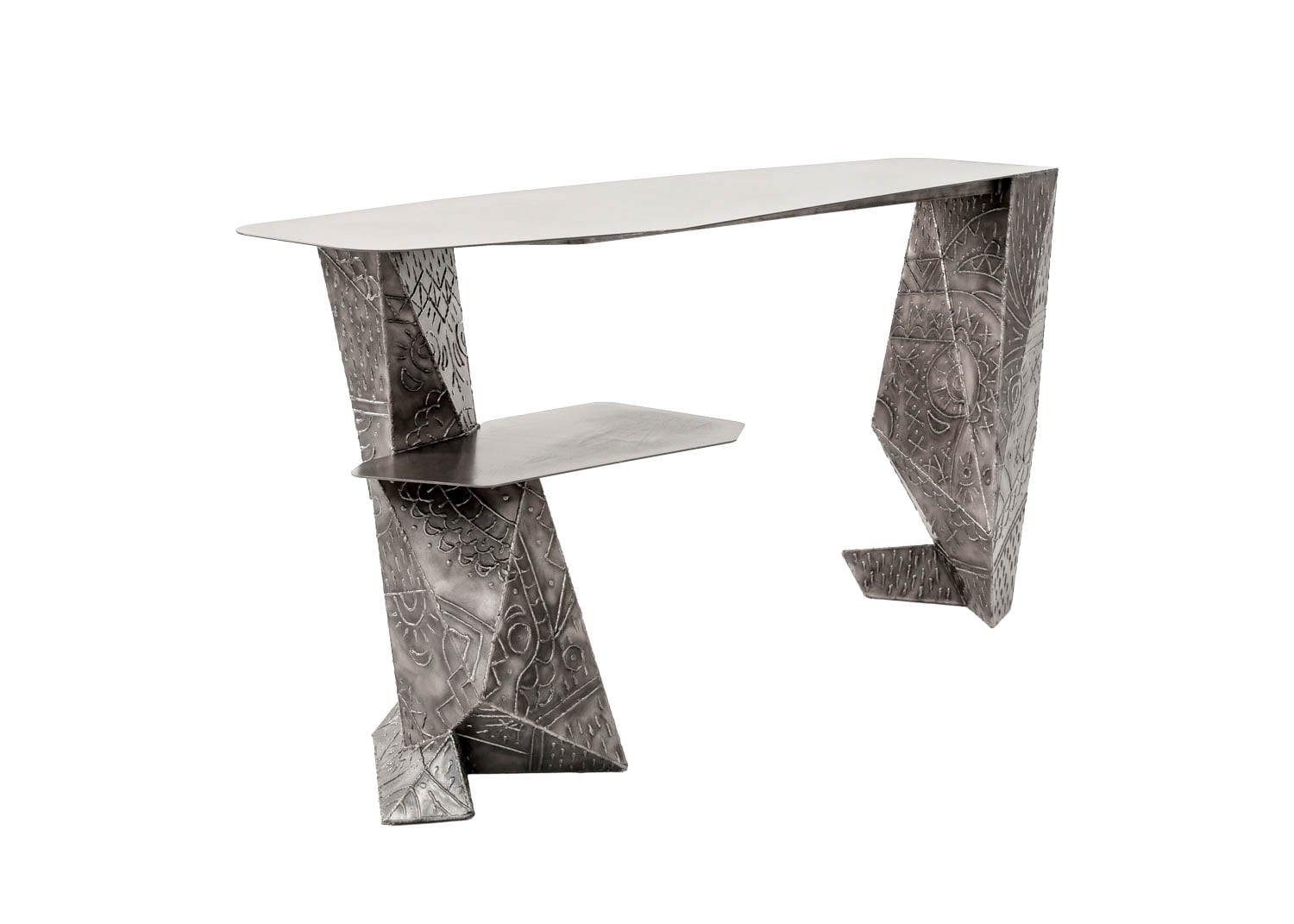 Asymmetrical metal desk with geometric legs and engraved patterns, featuring a small angled shelf beneath the tabletop.