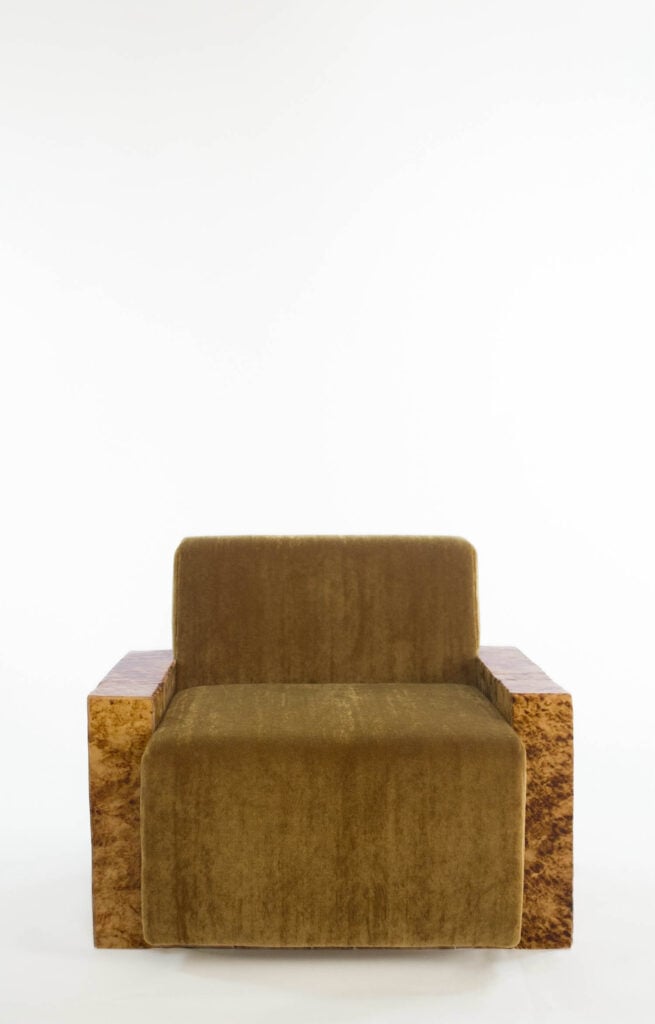 A brown velvet armchair with straight lines and wide, textured wooden armrests, photographed against a plain white background.
