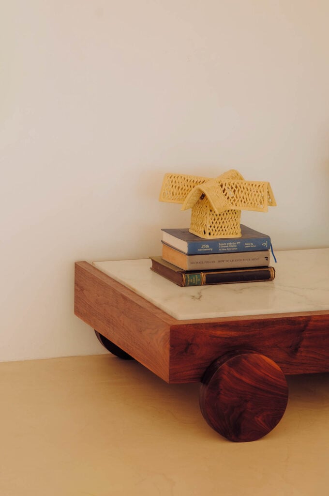 A wooden table with a marble top holds a stack of books and a decorative woven object shaped like a bow.