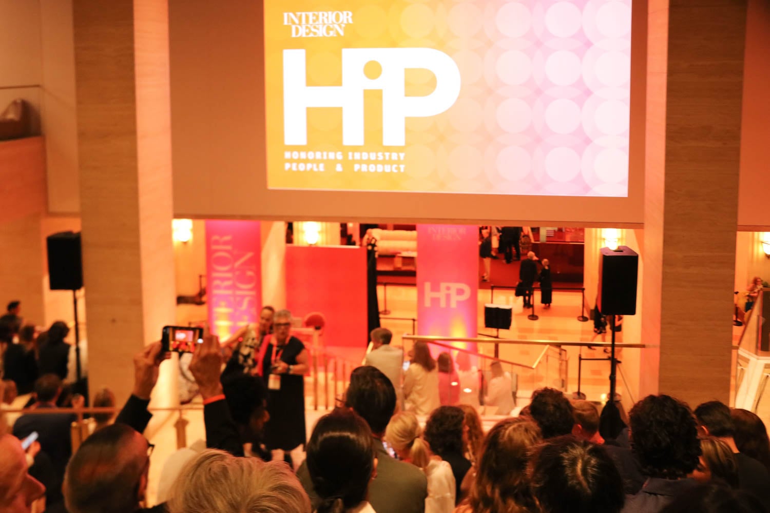 A crowd gathers at an indoor event with a large screen displaying "HiP: Honoring Industry People & Product" by Interior Design magazine.