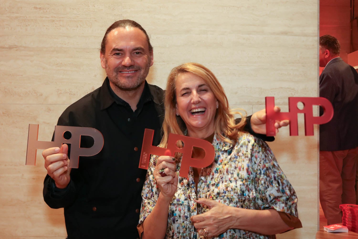 Two people smiling and holding up red and silver "HIP" signs at an indoor event.