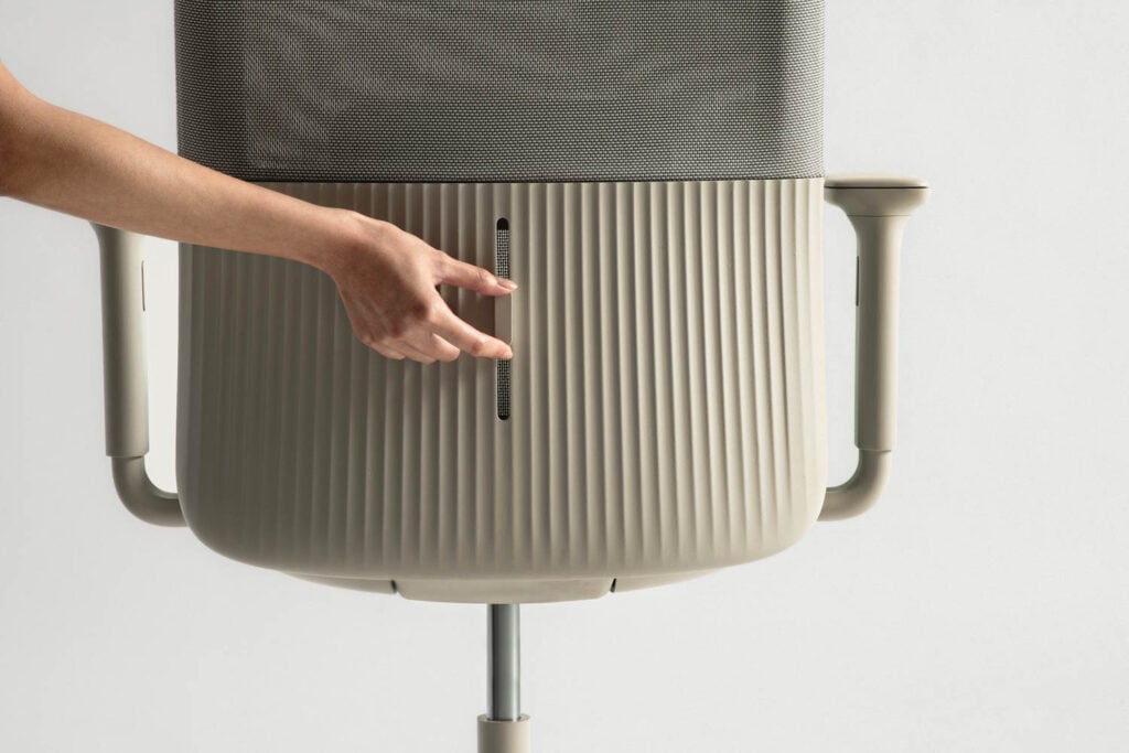 A person adjusts the vertical slider on the back of a beige office chair with a ribbed design and mesh backrest.