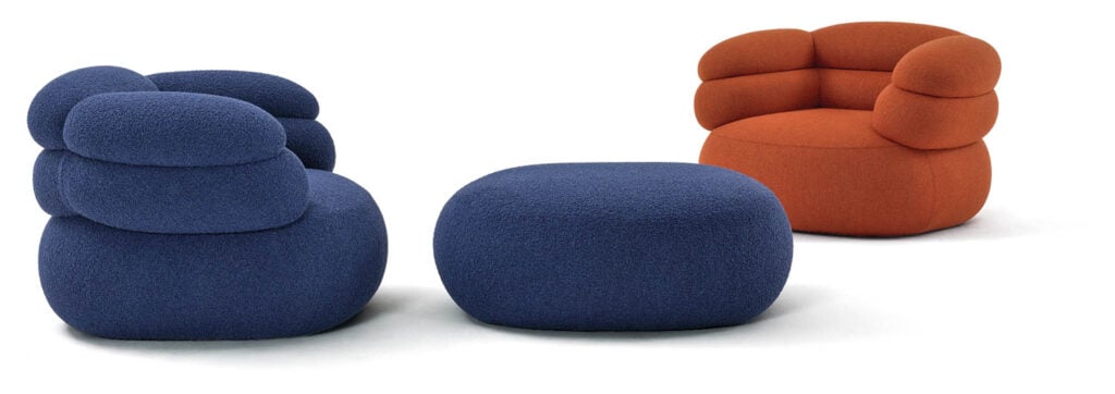 Two modern, rounded armchairs—one blue, one orange—alongside a matching blue ottoman, all upholstered in a textured fabric, set against a white background.
