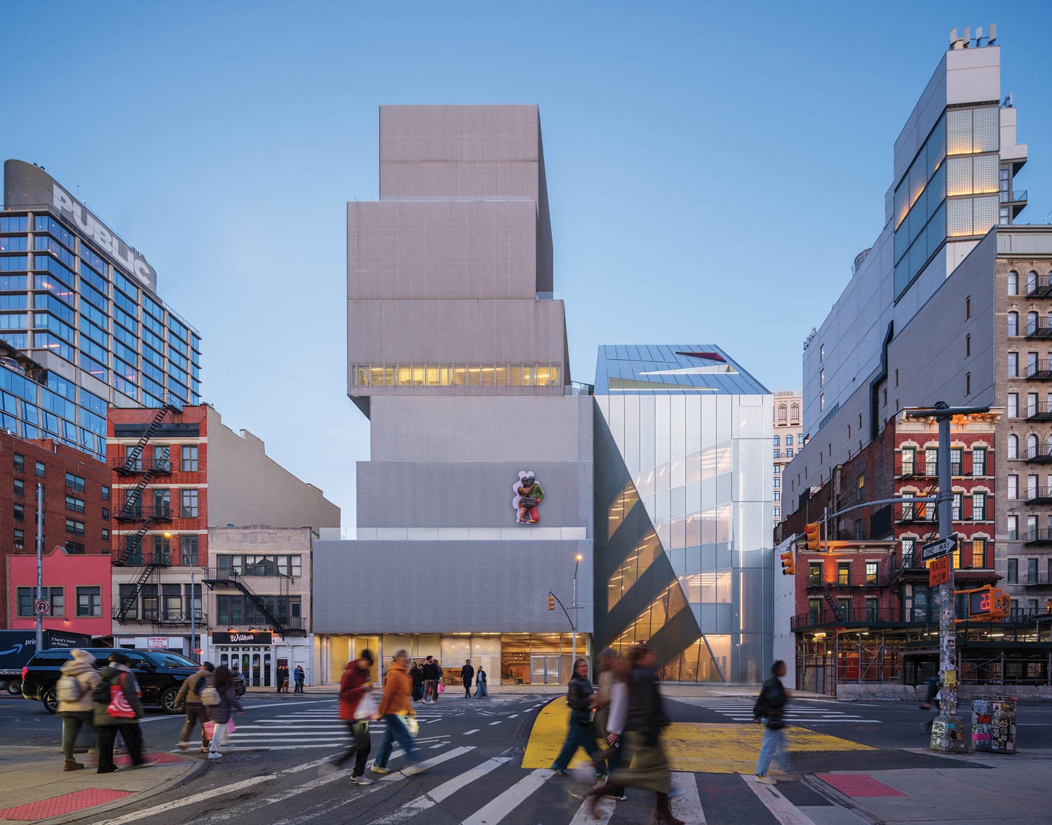 A modern, boxy museum building with stacked rectangular sections stands at a city intersection, surrounded by pedestrians and older brick buildings.