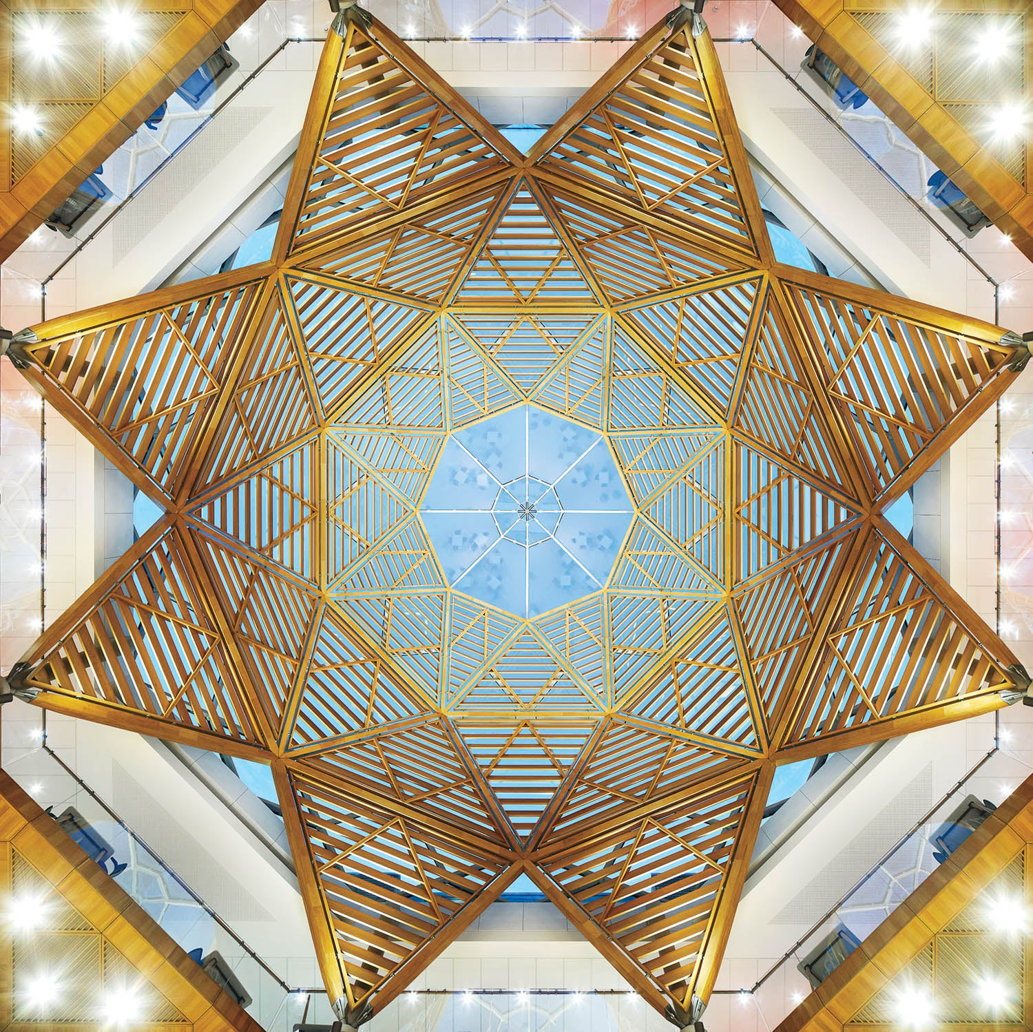 Geometric ceiling structure with wooden beams forming a symmetrical star pattern, viewed from below, with skylight in the center.