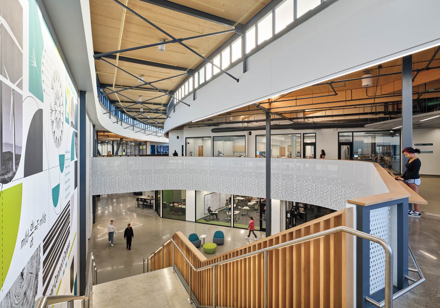 Modern office interior with open common areas, glass-walled offices, a large mural, and people walking and working on both floors.