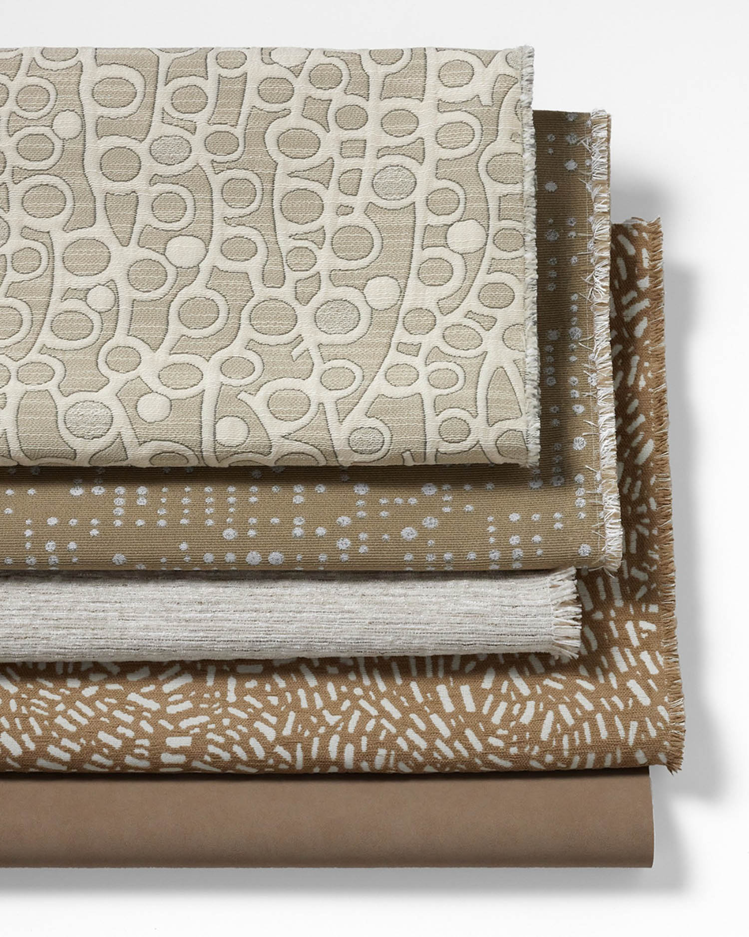 A stack of five folded fabrics in neutral tones, each featuring different textured or patterned designs, arranged on a white background.