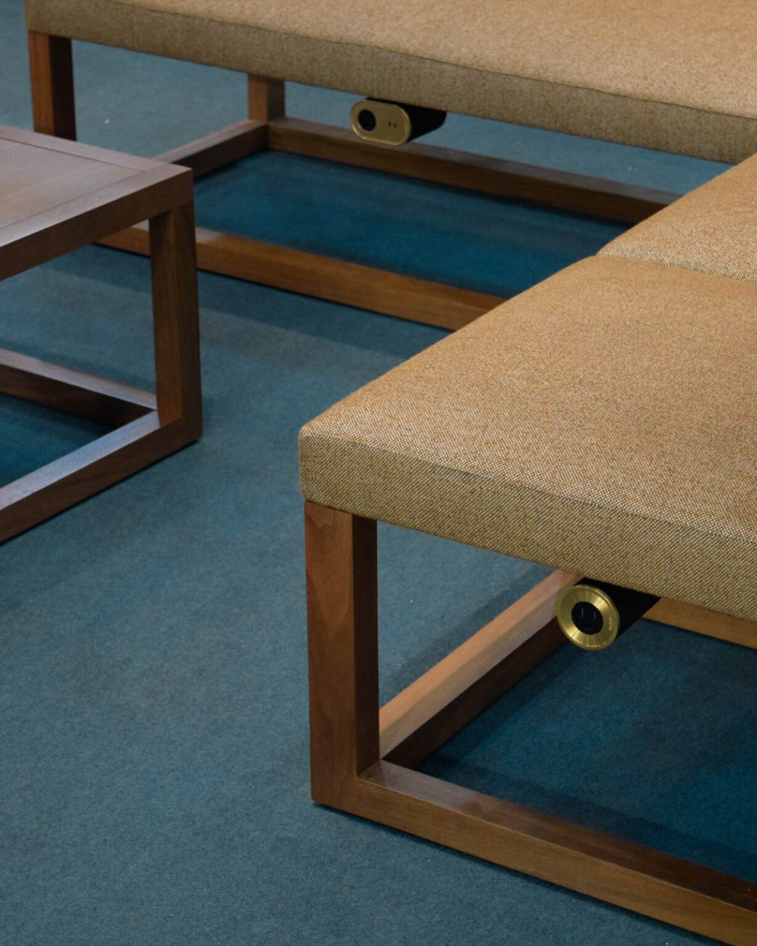 Rectangular wooden benches with tan upholstered seats and a matching wooden side table on a blue carpeted floor.