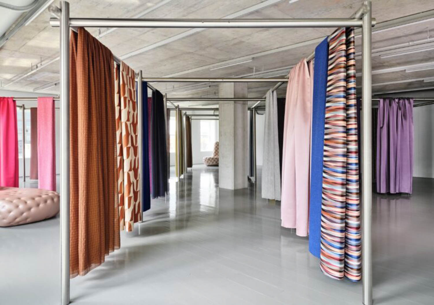 Several colorful fabric panels hang from metal frames in a spacious, modern room with concrete ceilings and glossy light gray floors.