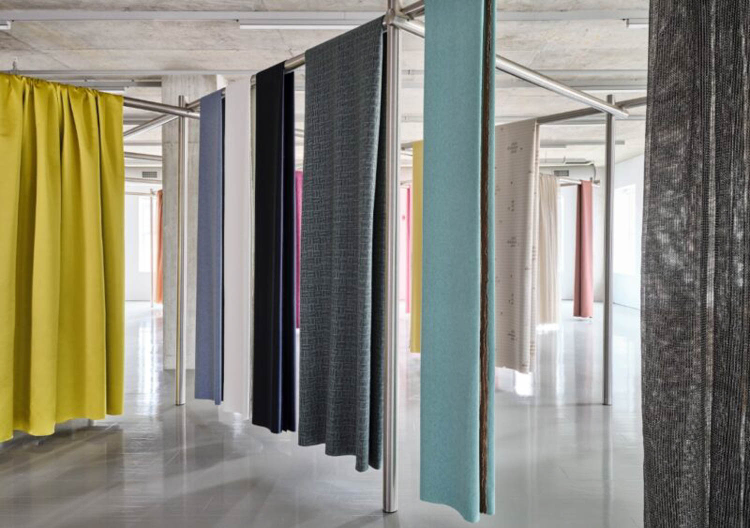 Multiple fabric panels in various colors and textures hang from metal rods in a modern, well-lit showroom.
