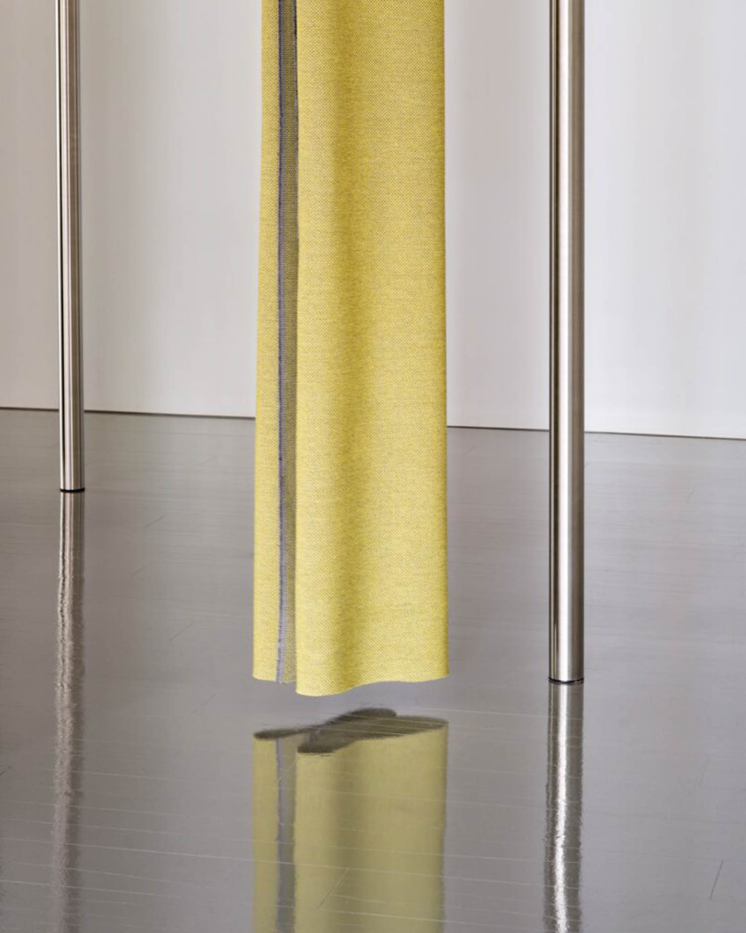 A yellow fabric curtain hangs between two metal poles, casting a reflection on a shiny gray floor.