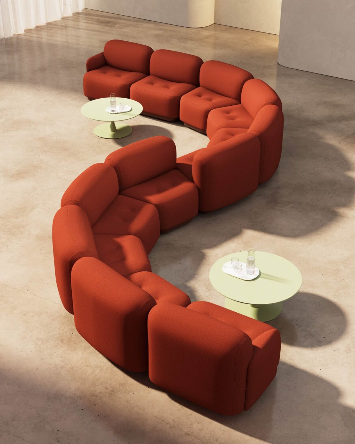 Curved modular red sofa set arranged in an S-shape around two round pale green coffee tables on a polished concrete floor.