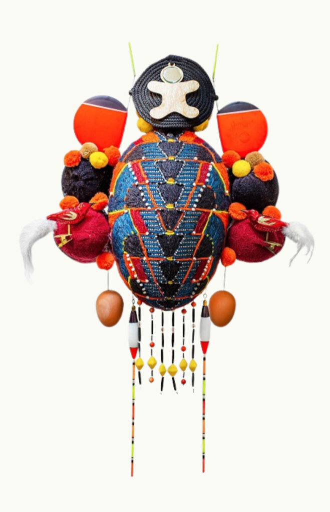 A colorful, abstract insect-like sculpture made from various materials including beads, pom-poms, fabric, and spherical objects, displayed against a plain white background.