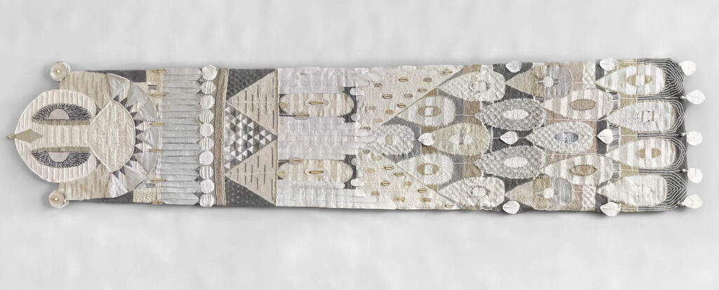 A rectangular textile artwork features geometric and symmetrical patterns in neutral tones, with white, gray, and beige shapes and textured details across its length.