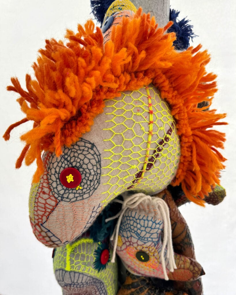 Close-up of three handmade fabric animal dolls with colorful yarn manes and embroidered details, stacked vertically against a plain white background—a charming creation reminiscent of Wolfgang Woerner's whimsical style.