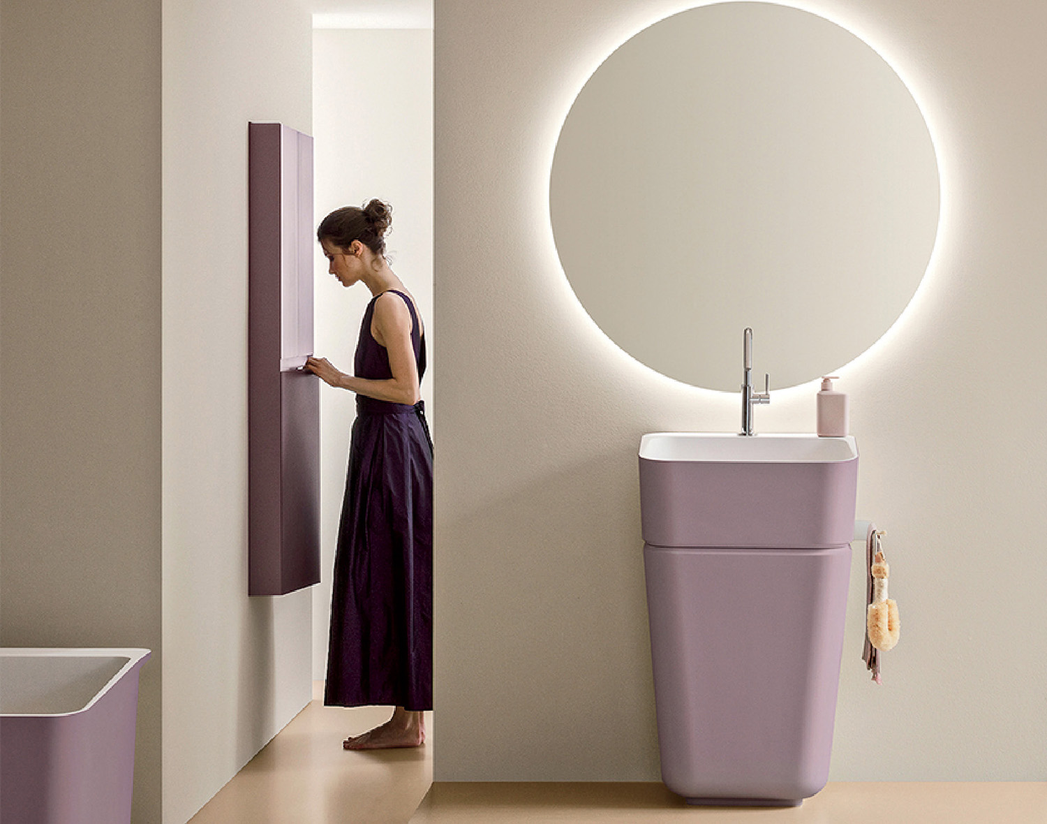 A woman in a sleeveless dress stands in a minimalist bathroom, interacting with a tall, narrow cabinet; a round mirror and lavender sink are visible.