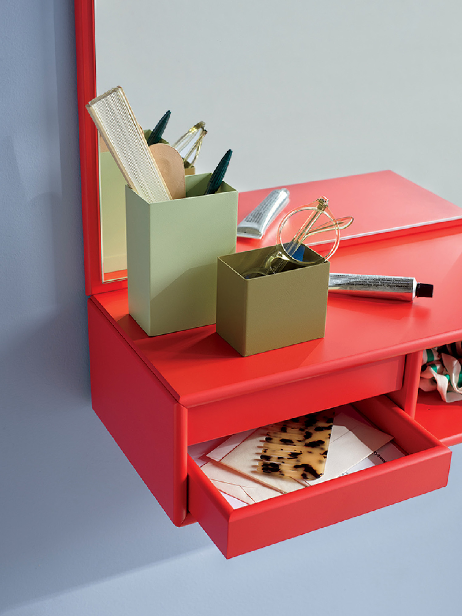 A red vanity with an open drawer holds a patterned handkerchief; green containers on top store books, pens, and decorative items.
