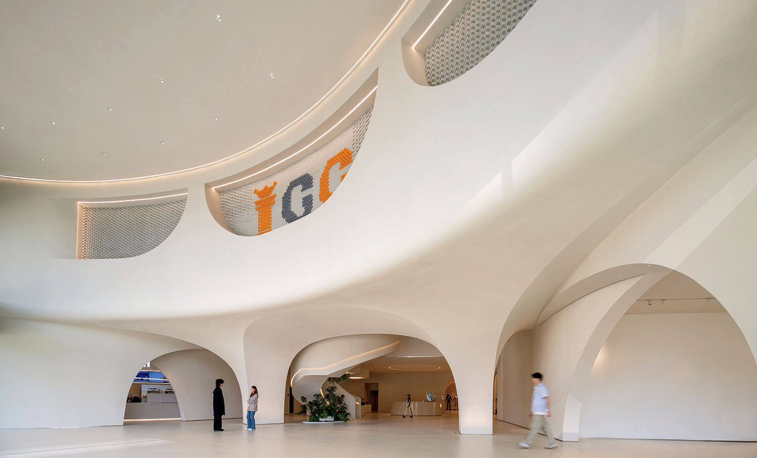 Spacious modern interior with curved white walls, large arches, and a few people walking or standing on the smooth floor.