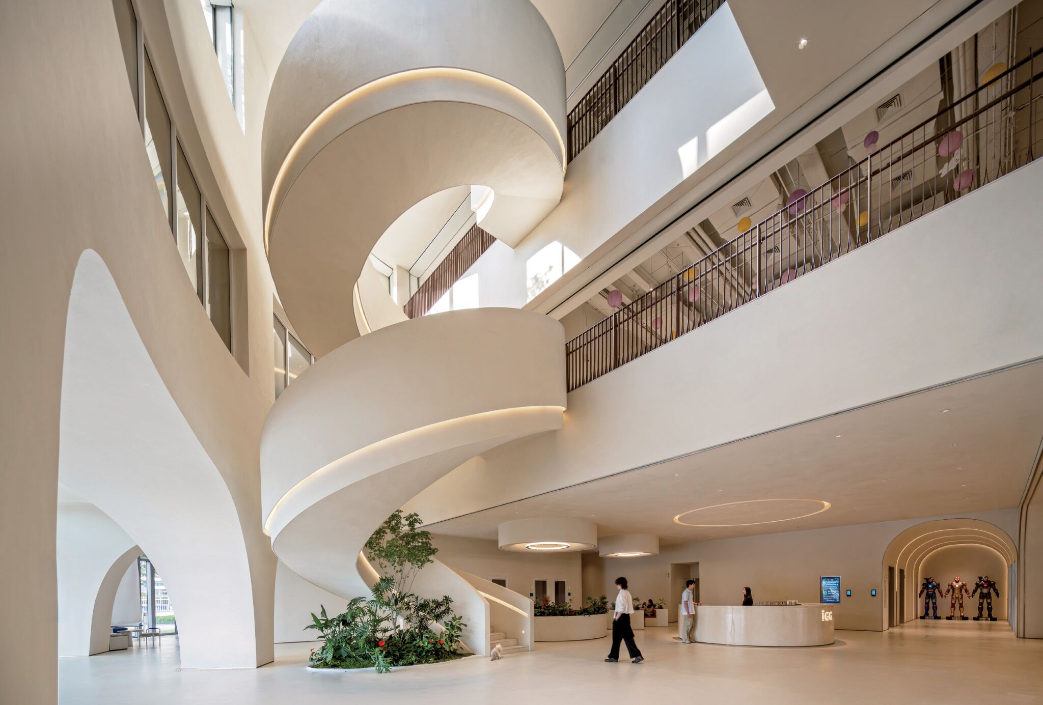 Spiral staircase and plants in a modern, spacious lobby with high ceilings, large windows, and people near a reception desk.