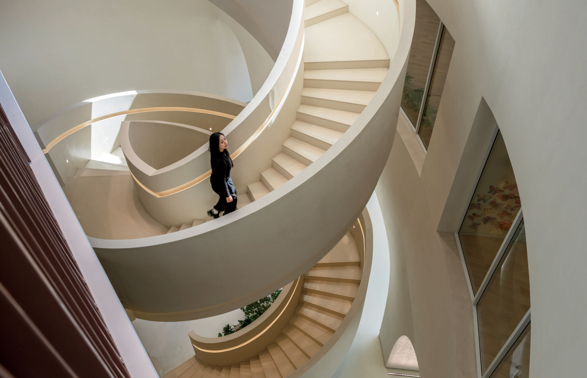 A person walks up a modern, spiral staircase with cream-colored steps and curved railings inside a well-lit building.
