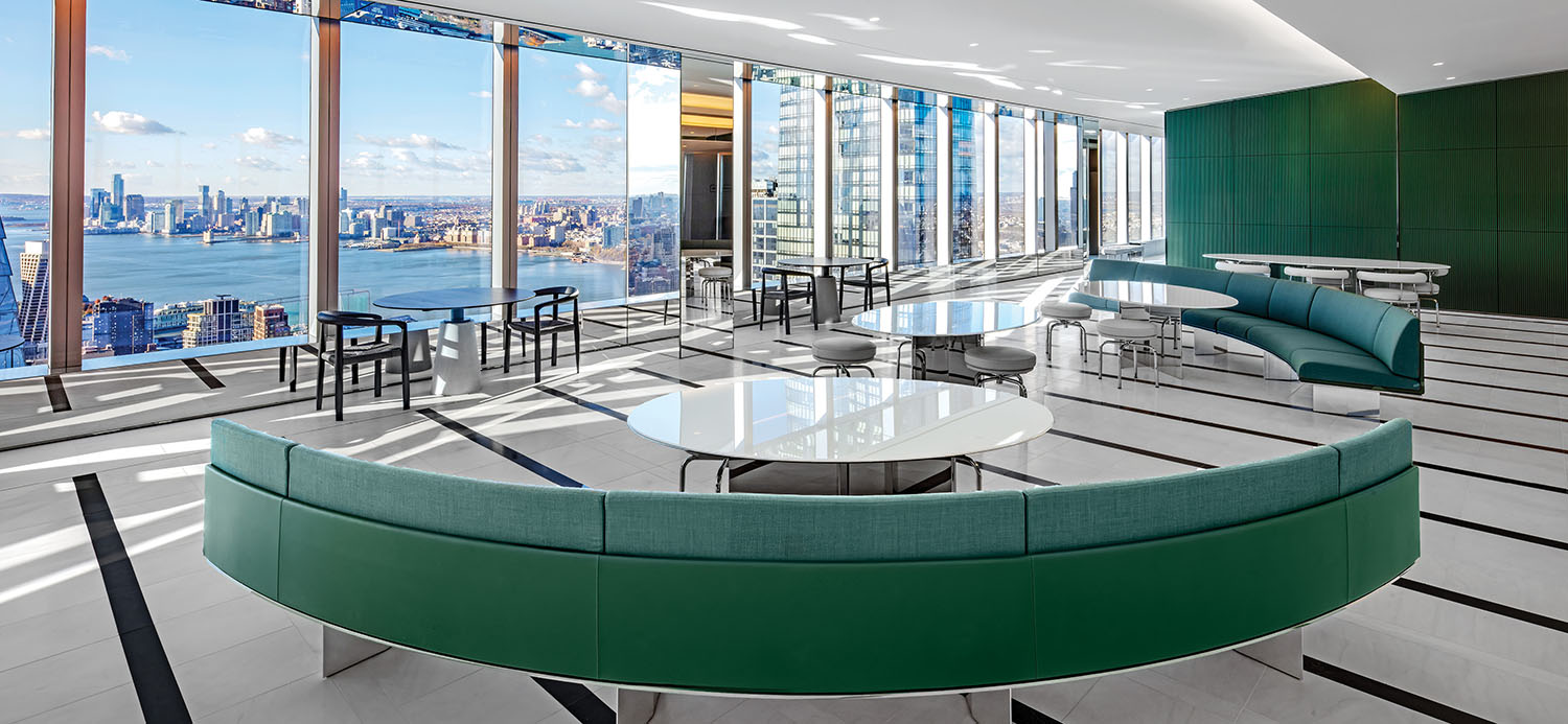 Modern lounge with green curved sofas, round tables, and floor-to-ceiling windows overlooking a city skyline and river.