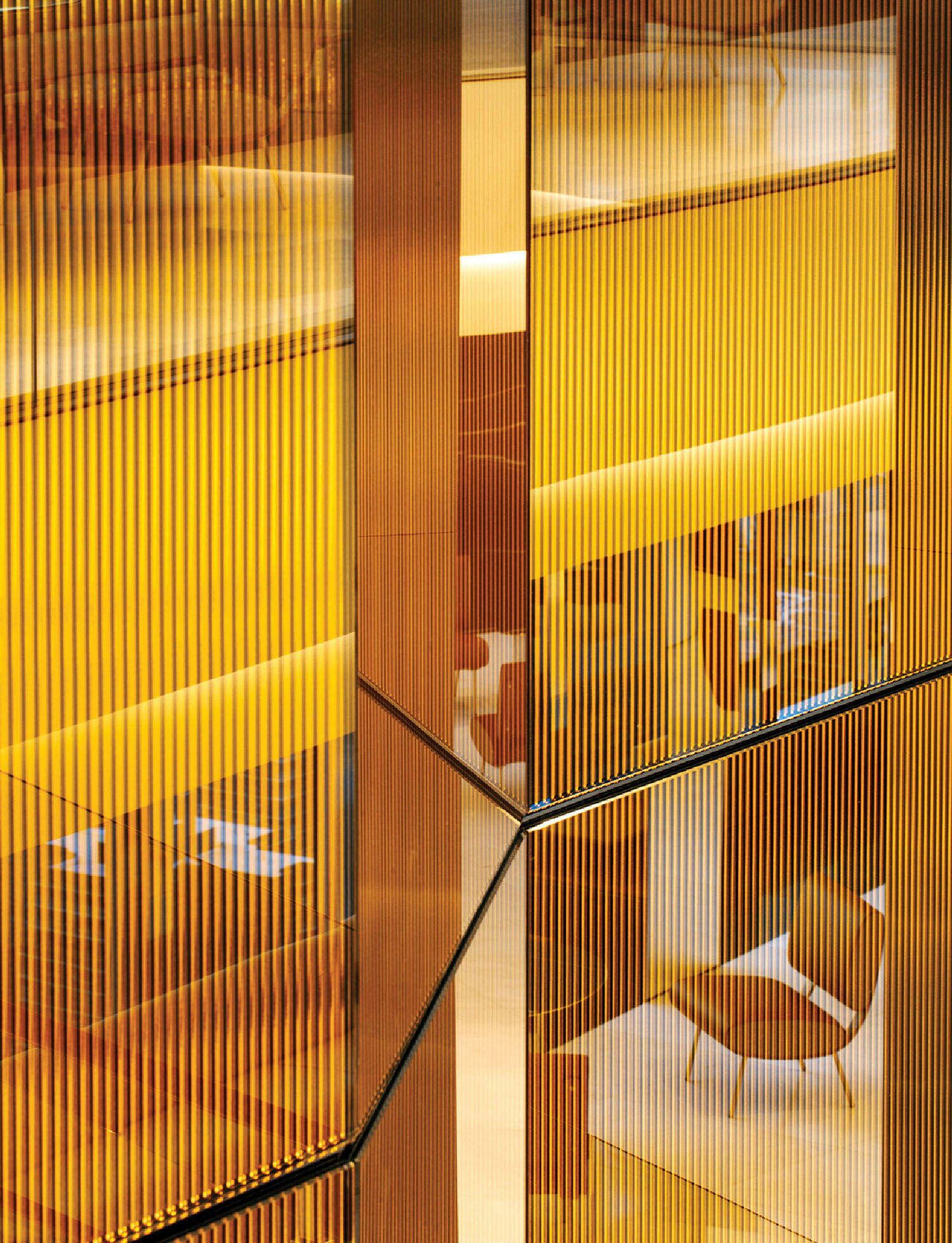 Geometric interior with golden vertical panels and glass, reflecting light and creating abstract patterns with yellow and brown tones.