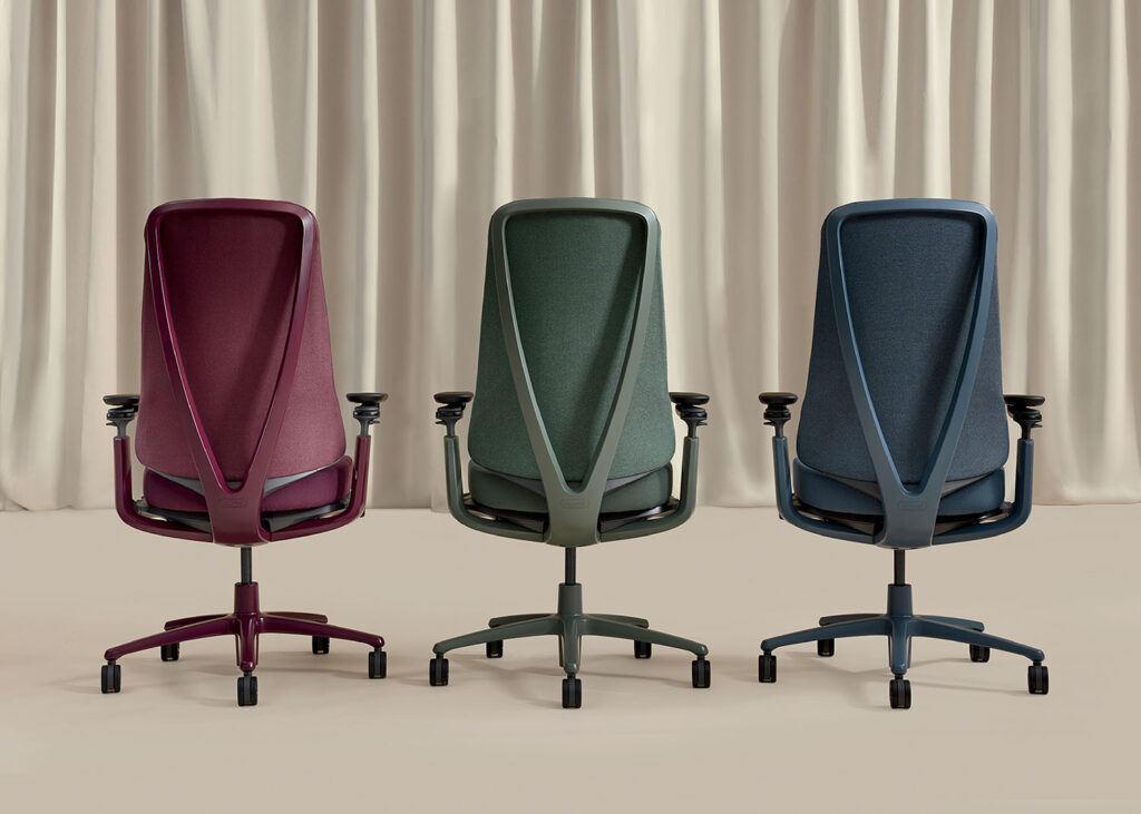 Three modern office chairs in burgundy, green, and blue are shown from the back against a beige curtain background.