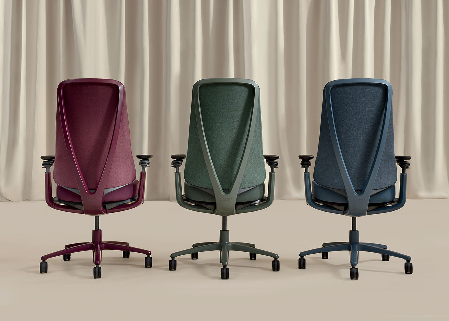 Three modern office chairs in burgundy, green, and blue are shown from the back against a beige curtain background.