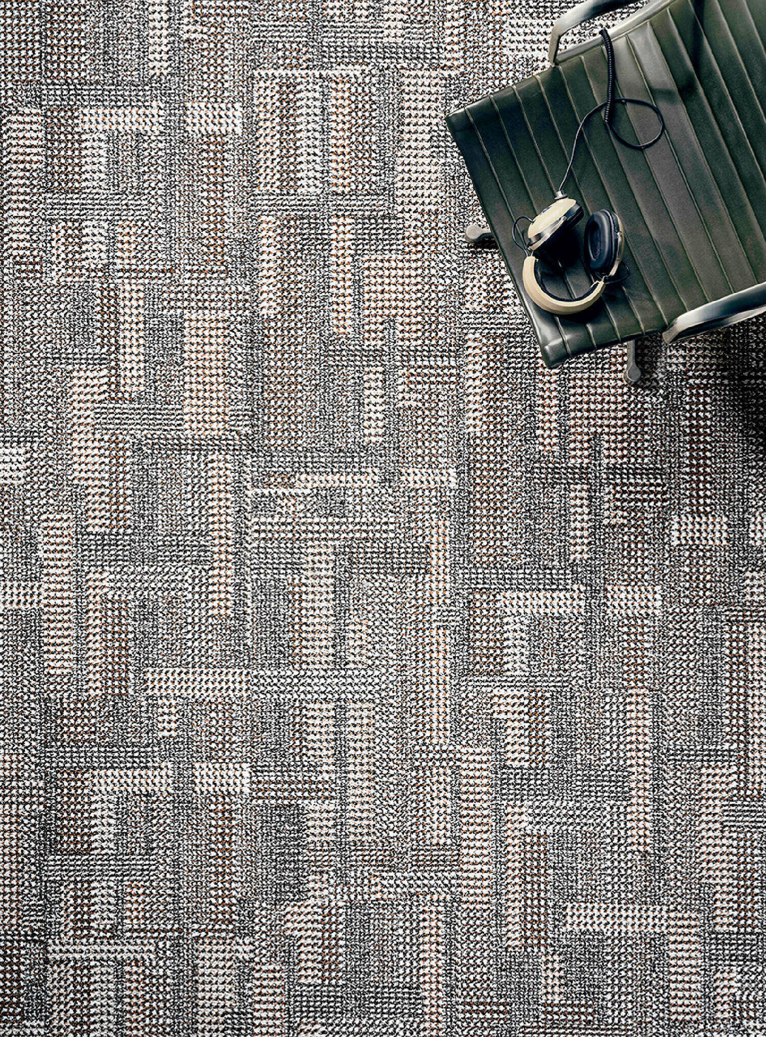 Overhead view of a green chair with headphones resting on it, positioned on a textured, woven-pattern carpet in neutral tones.