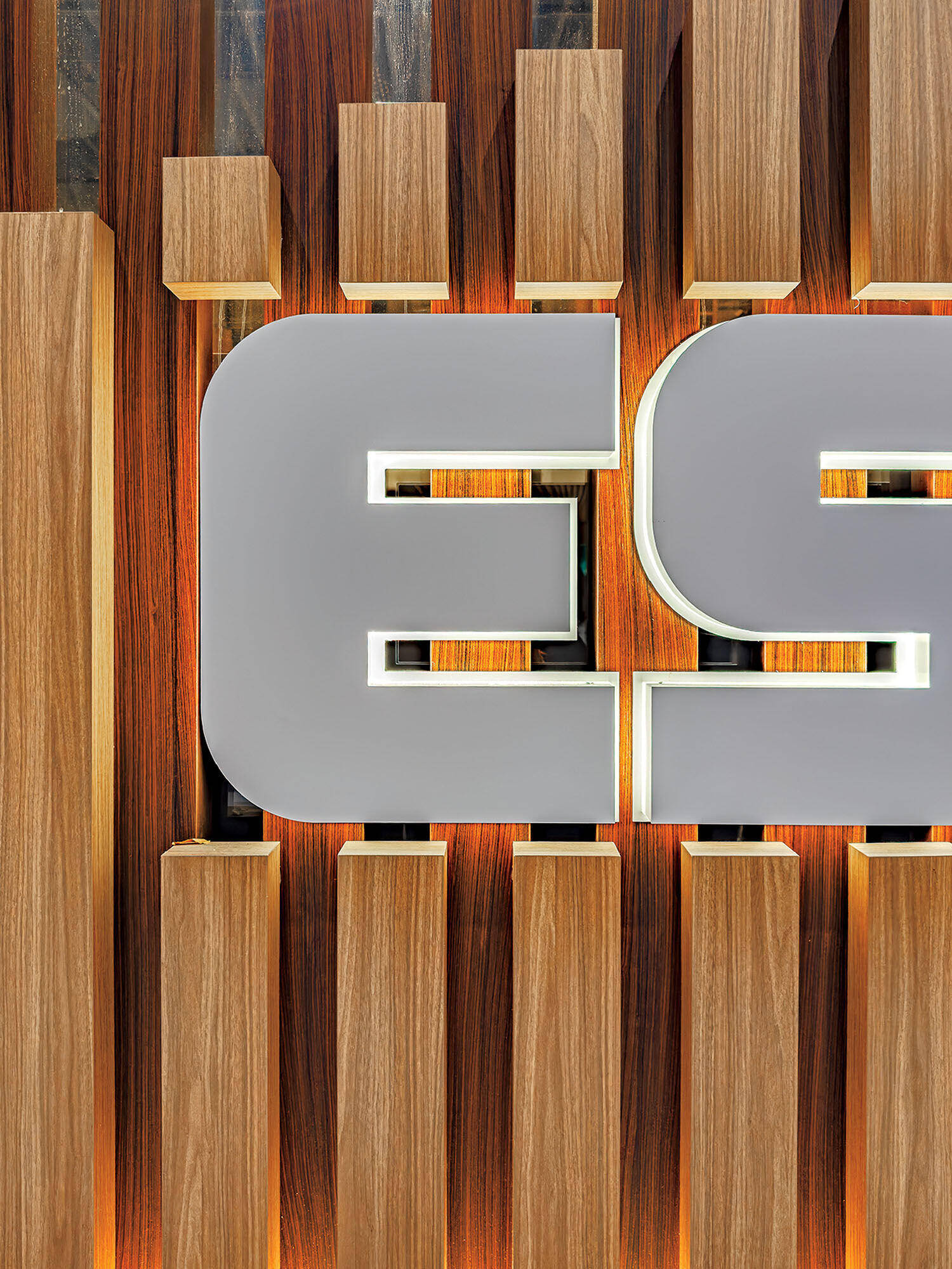 Close-up of a wall featuring vertical wooden slats and a large, illuminated gray letter "E" as part of a sign or logo.