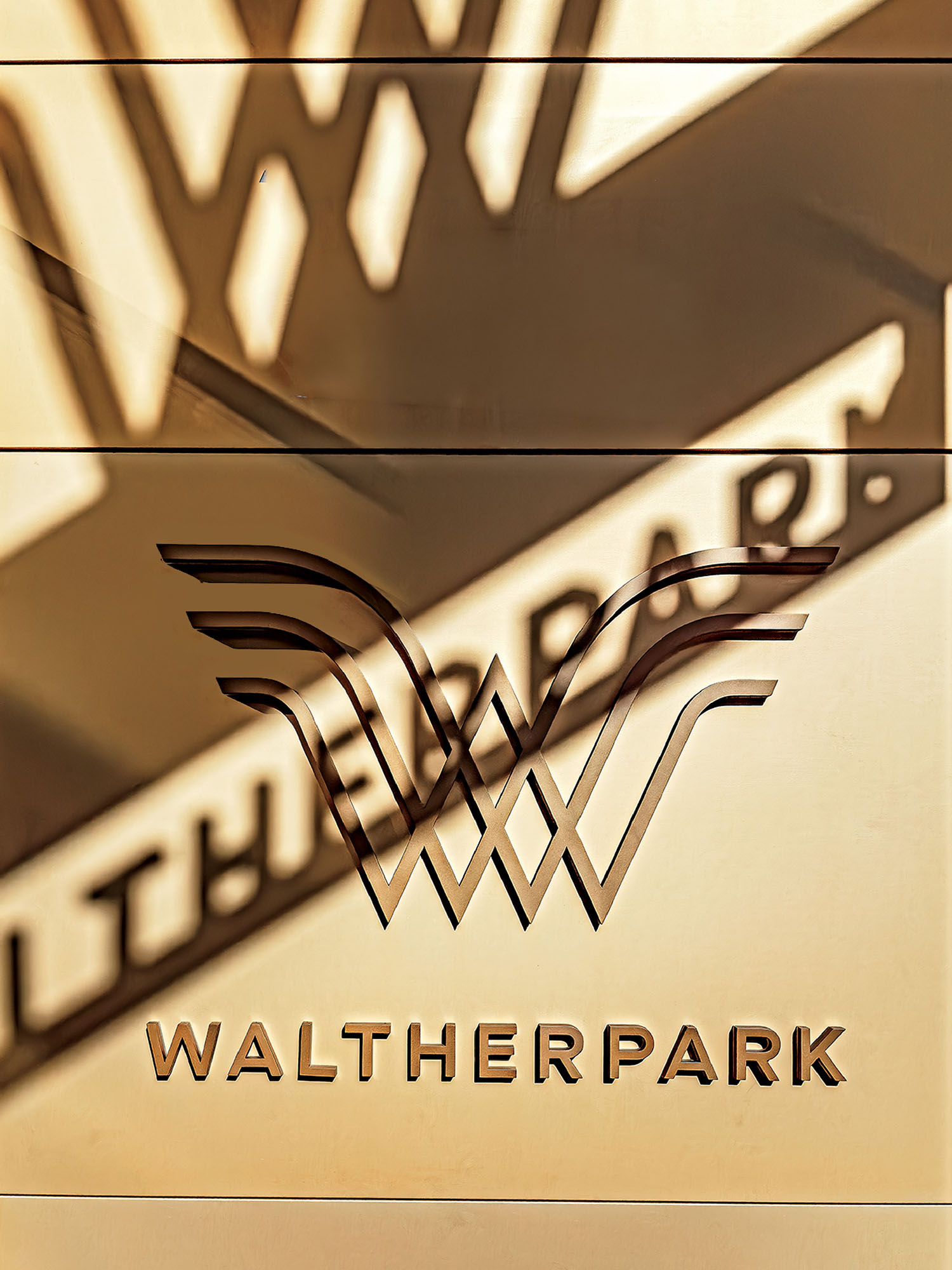 Metallic sign with the stylized word "WALTHERPARK" and a double W logo, with the design casting a shadow on the wall behind it.