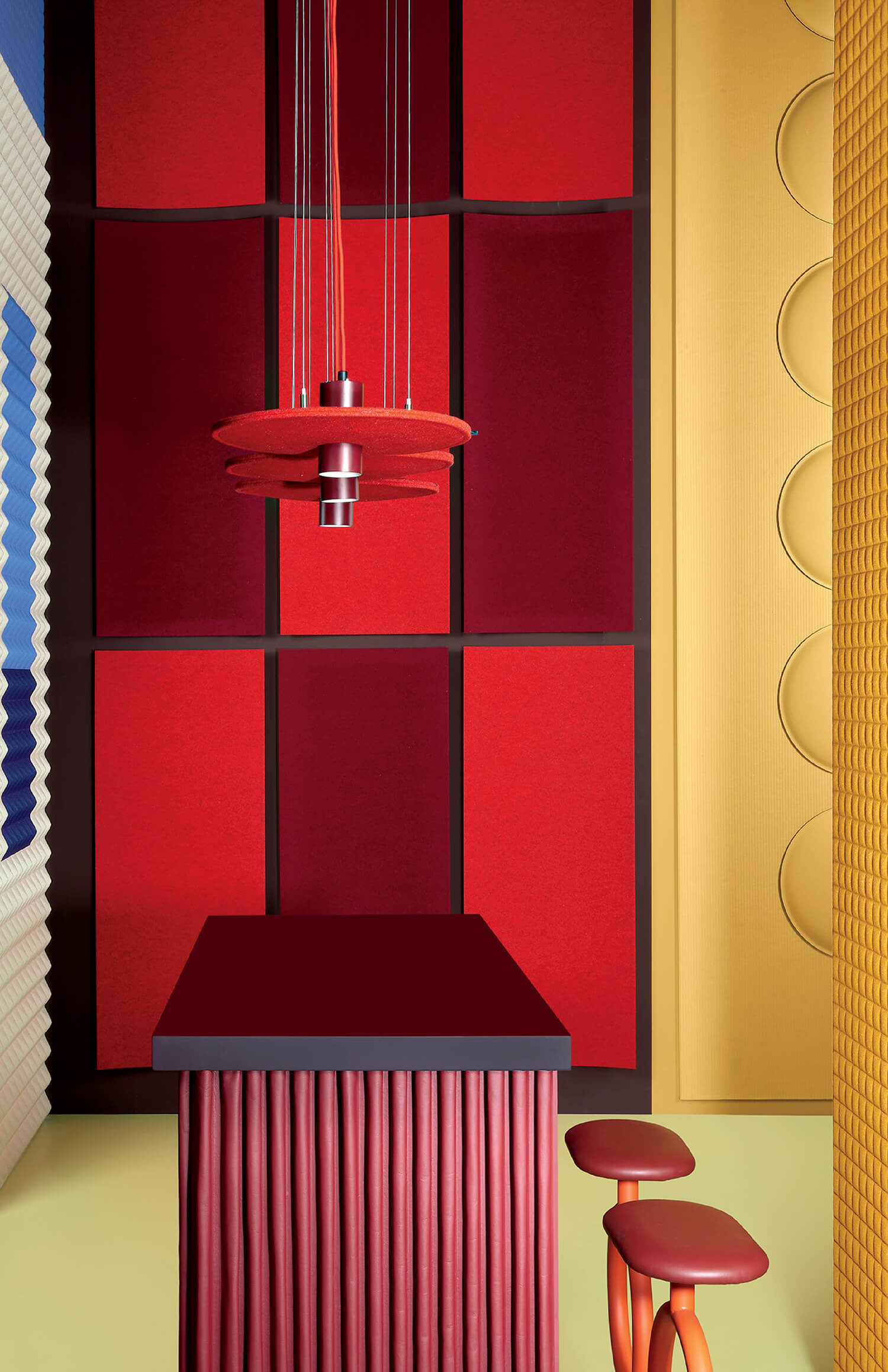 A modern room with red and burgundy panel walls, a matching red table and stools, a red pendant light, and yellow textured walls.