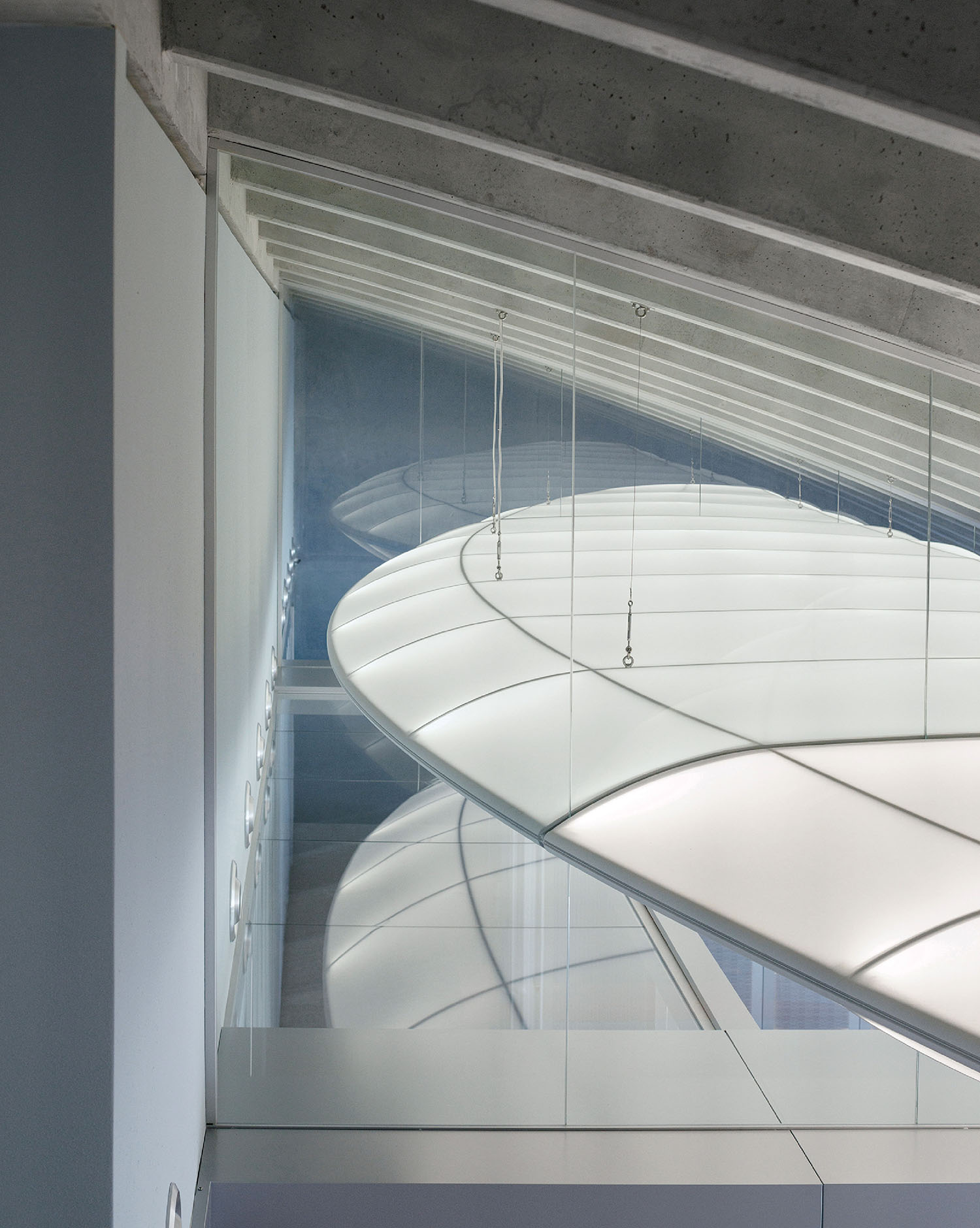 Interior view of a modern building featuring curved, translucent ceiling panels, glass walls, and exposed concrete beams.