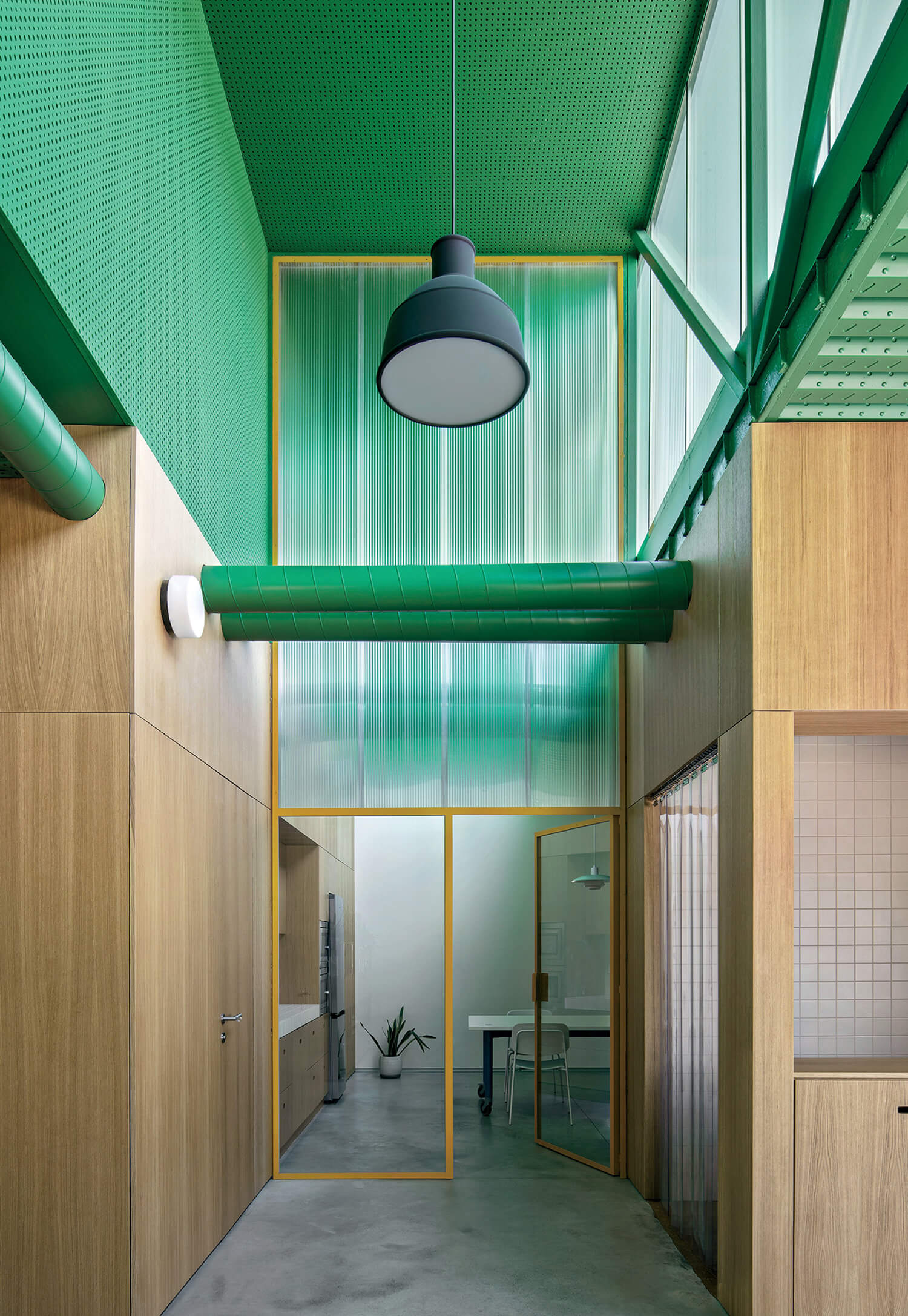 Modern interior with green ceiling, wood-paneled walls, large pendant light, glass doors, and an open workspace visible in the background.