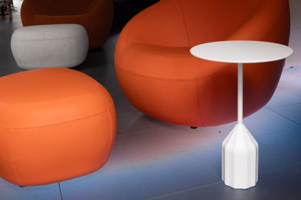 Modern lounge with an orange armchair, matching orange ottoman, small round white side table, and a light gray ottoman on a tiled floor.