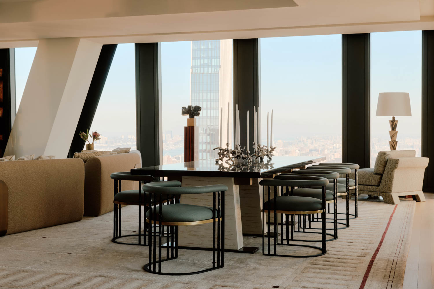 Modern dining and living area with floor-to-ceiling windows, city skyline view, neutral furnishings, a dark table, eight chairs, a sofa, armchair, and a tall floor lamp.