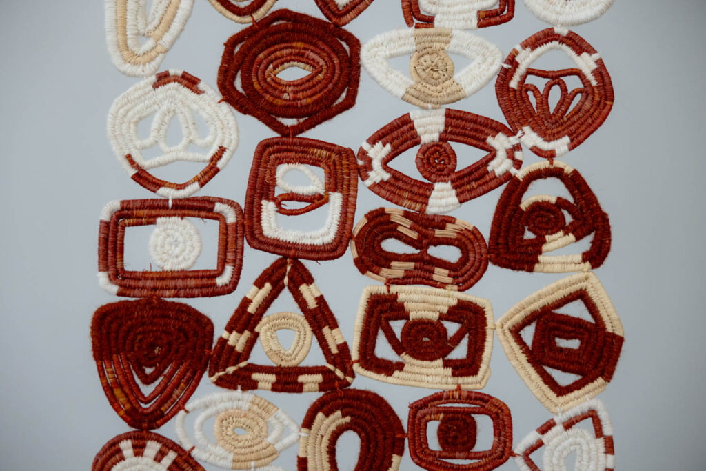 A collection of woven geometric shapes in red, beige, and white, arranged closely together on a plain light gray background.